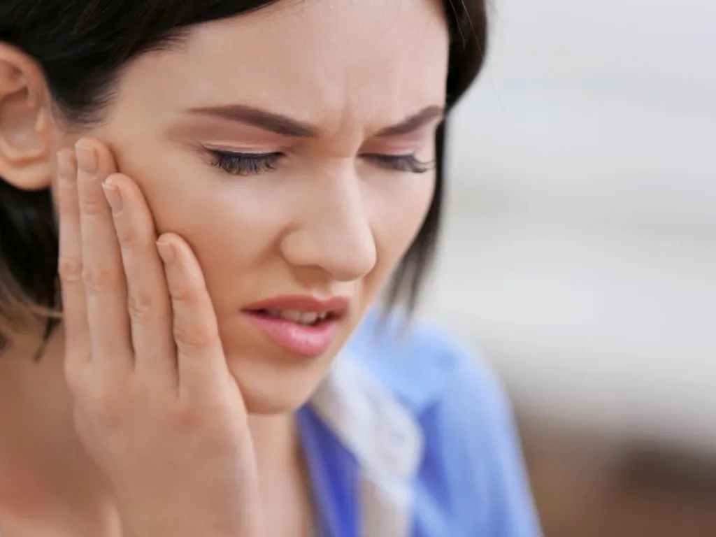 Young woman experiencing dental pain and holding her jaw, a common symptom of a failed root canal. Persistent pain, swelling, and sensitivity can indicate infection or treatment failure.