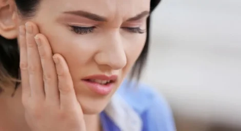 Young woman experiencing dental pain and holding her jaw, a common symptom of a failed root canal. Persistent pain, swelling, and sensitivity can indicate infection or treatment failure.